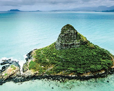Aerial view of a lush green island surrounded by turquoise waters under a cloudy sky.