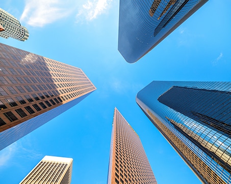 Upward view of several tall skyscrapers in downtown Los Angeles against a bright blue sky.